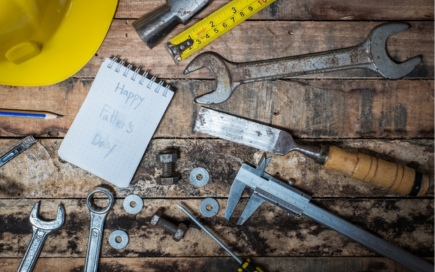 Tools, including wrenches and a caliper, lie scattered on a wooden surface. A yellow hard hat and notepad with 