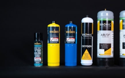 Various gas canisters stand upright against a dark background, featuring different brands like Bernzomatic and Bromic, with labels indicating contents, including MAPP, oxygen, and AR/O2.
