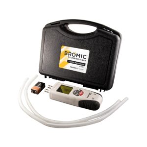 A digital manometer with tubes and a battery lies next to a black carrying case labeled "Bromic Plumbing & Gas Digital Manometer." The setup is for measuring pressure.